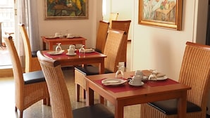 Ein Essbereich mit Korbstühlen und Tischen, zwei Bildern an den Wänden und einem Deckenventilator.