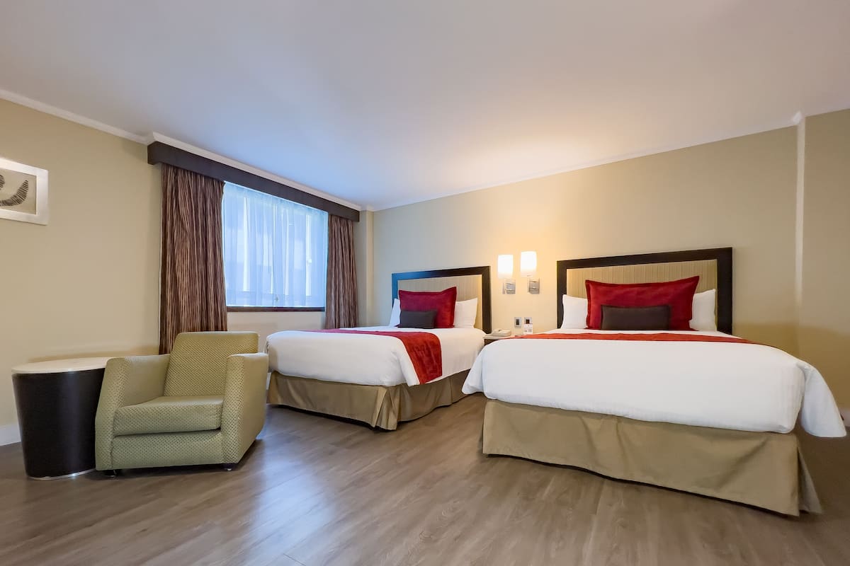 A hotel room with two beds, a chair, a bedside table, and a window with curtains.