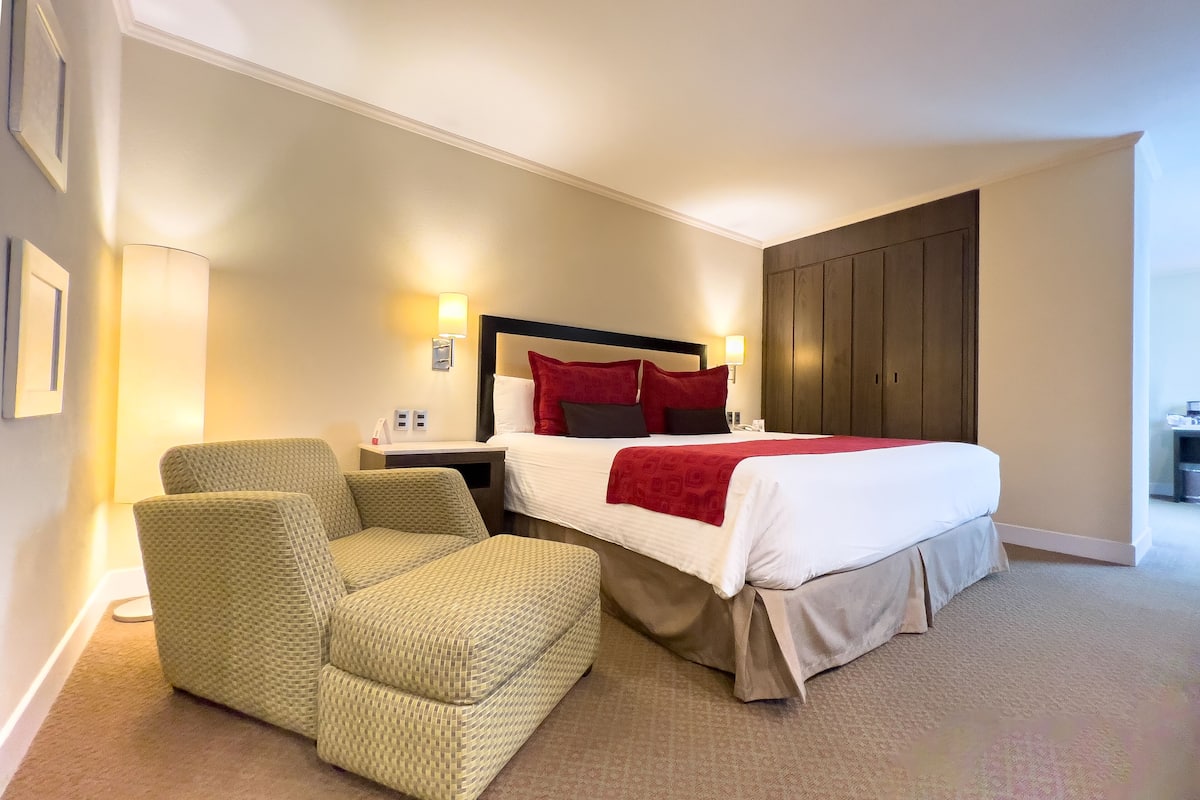 A hotel room with a bed, two armchairs, a nightstand, and a wardrobe.