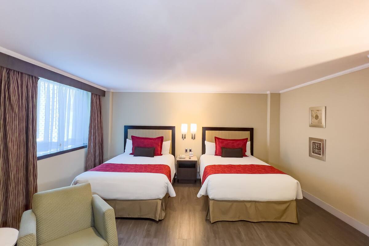 A hotel room with two beds, a chair, and a nightstand.