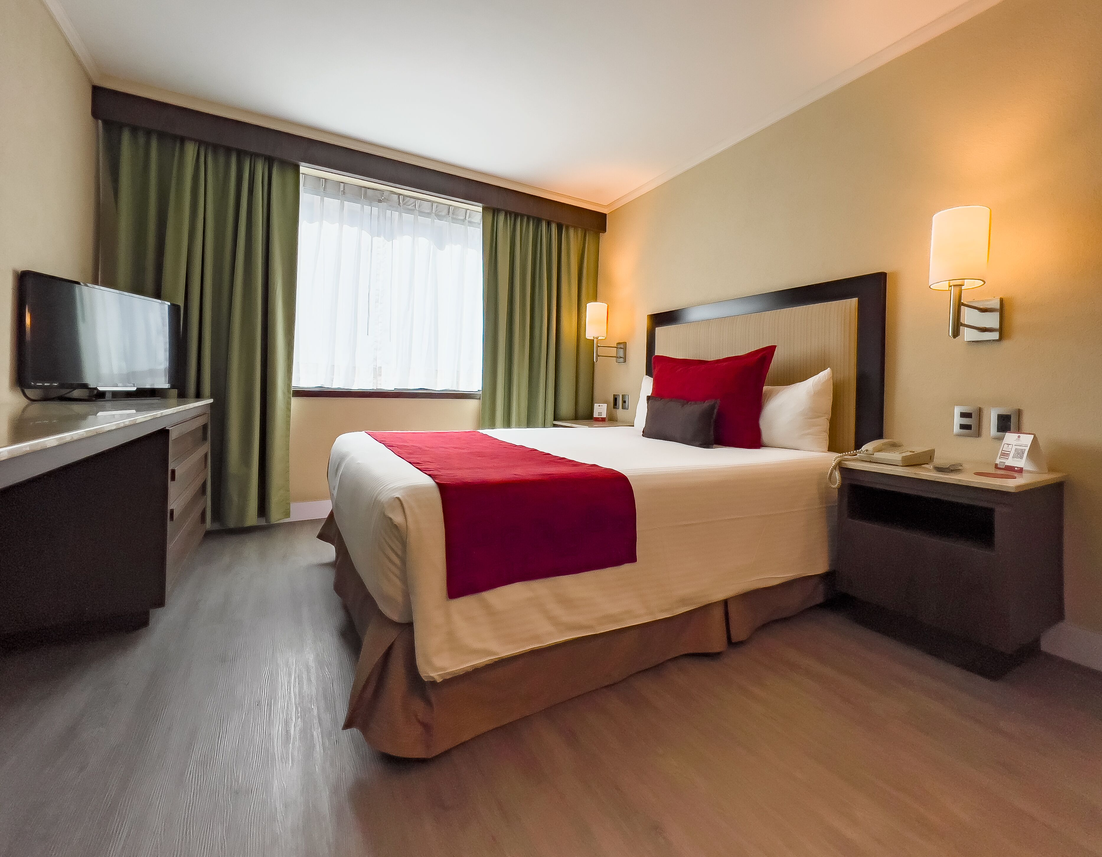 Una camera d'albergo con un letto, comodini, televisione e una finestra con tende.