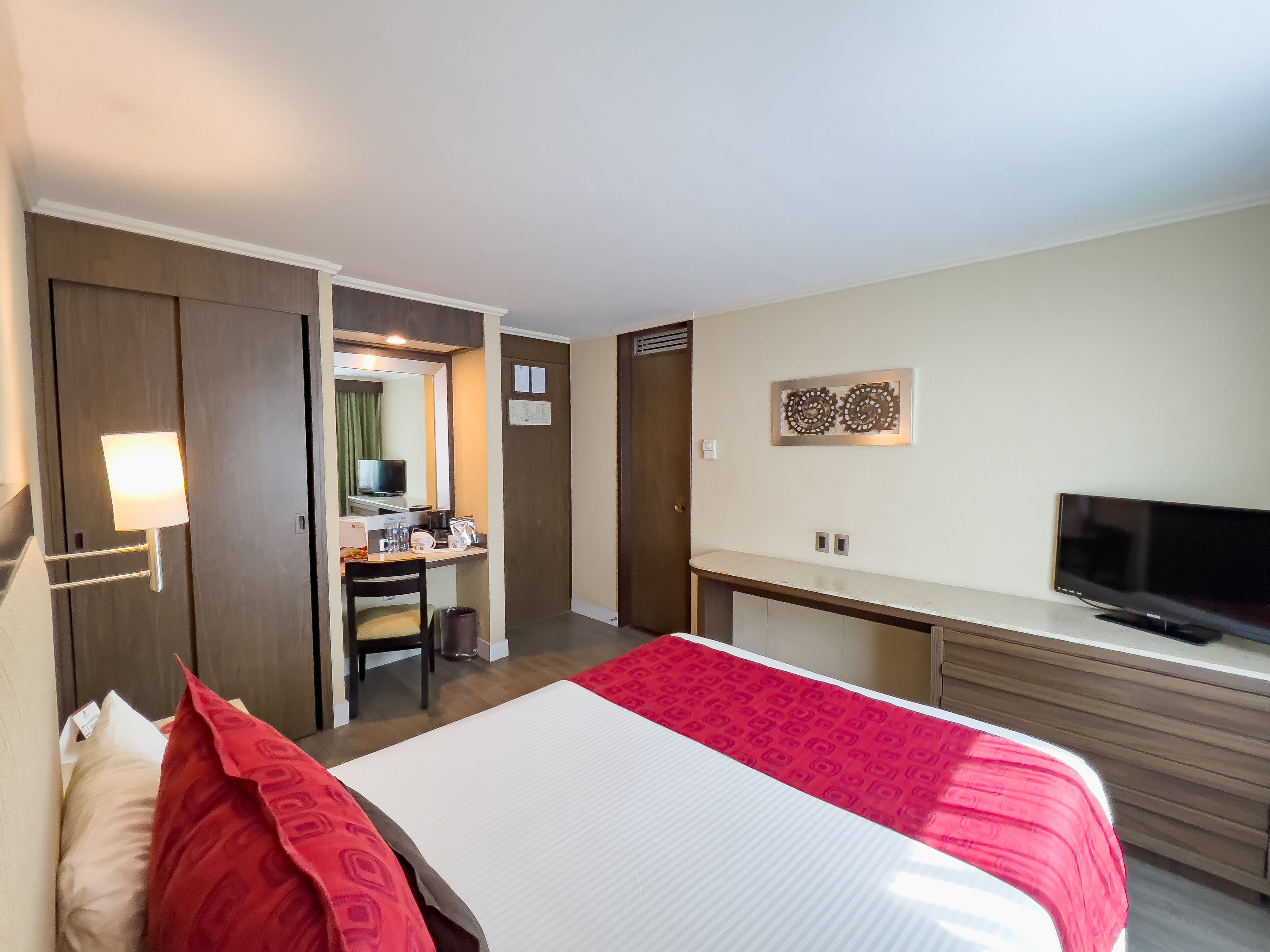 Una habitación de hotel con cama, escritorio, silla, televisor y una pequeña kitchenette.
