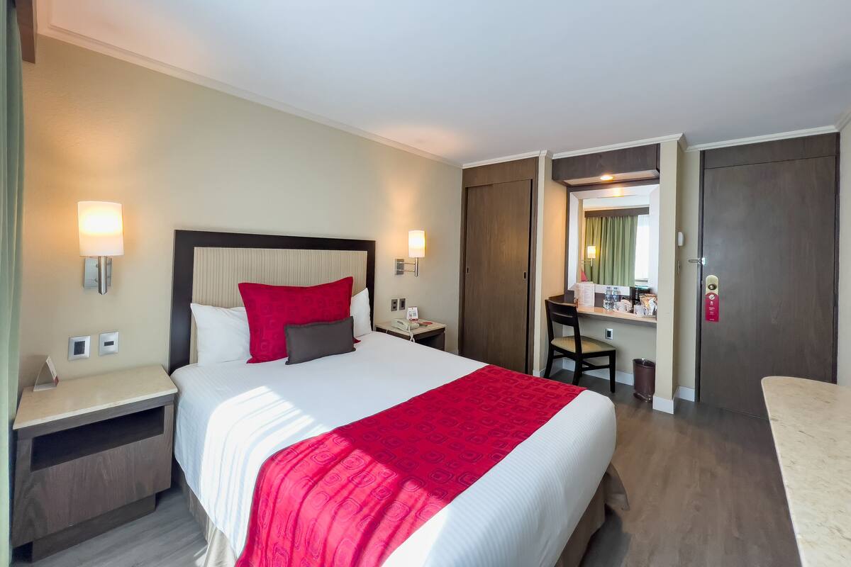 A hotel room with a large bed, bedside tables, a desk, and a wardrobe.