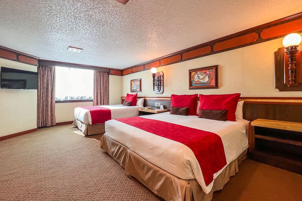 A hotel room with two beds, a flat-screen TV, a desk, and a window with curtains.