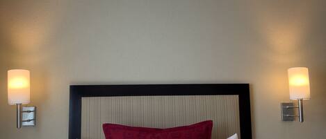 A hotel room with a large bed, two bedside lamps, a telephone, and a wall-mounted light switch.