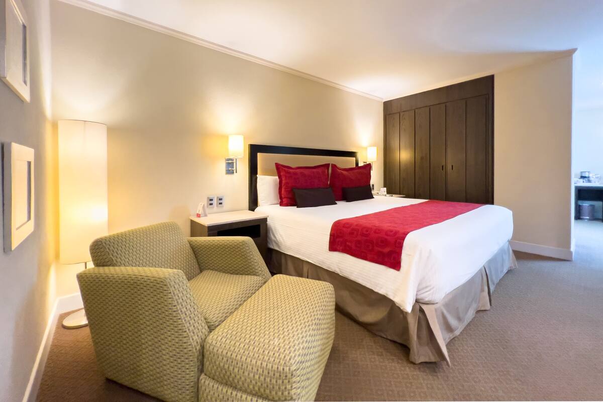 A hotel room with a bed, two armchairs, a nightstand, a lamp, and a wardrobe.