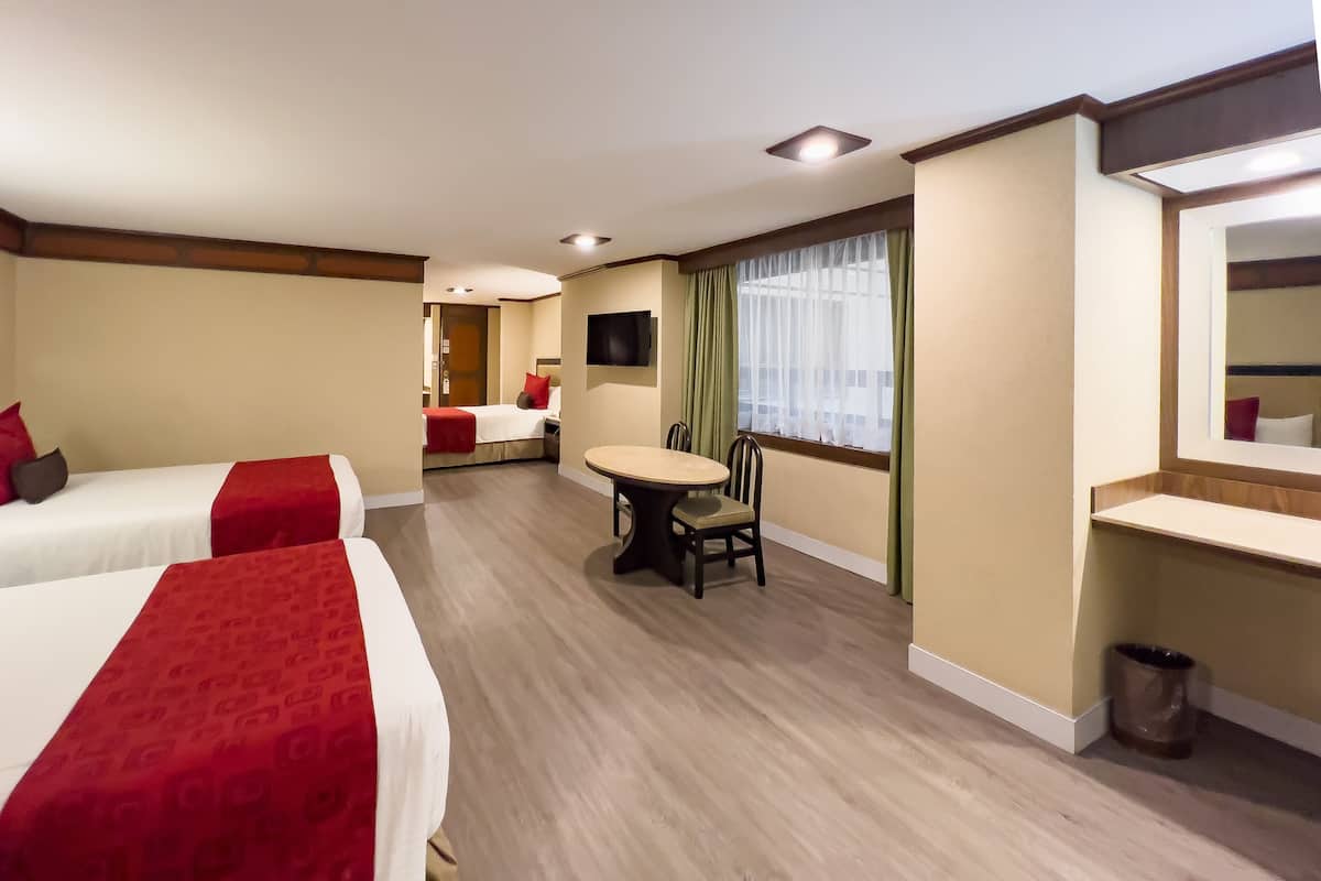 A hotel room with two beds, a dining table, a TV, and a window with curtains.