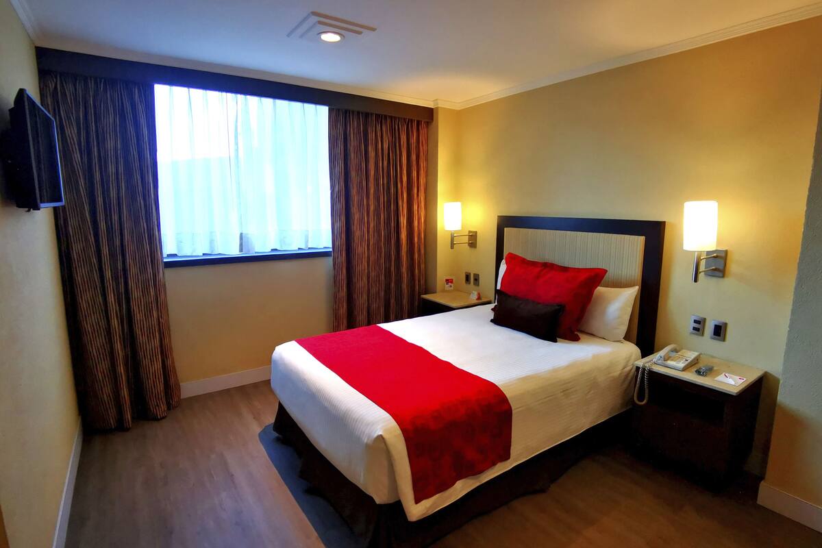 A hotel room with a large bed, a bedside table with a phone, and a window with curtains.