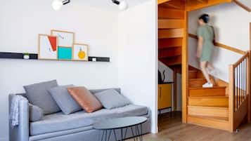 En moderne stue med en grå sofa, et lille bord, en trappe til et lavere niveau og en loftlampe.