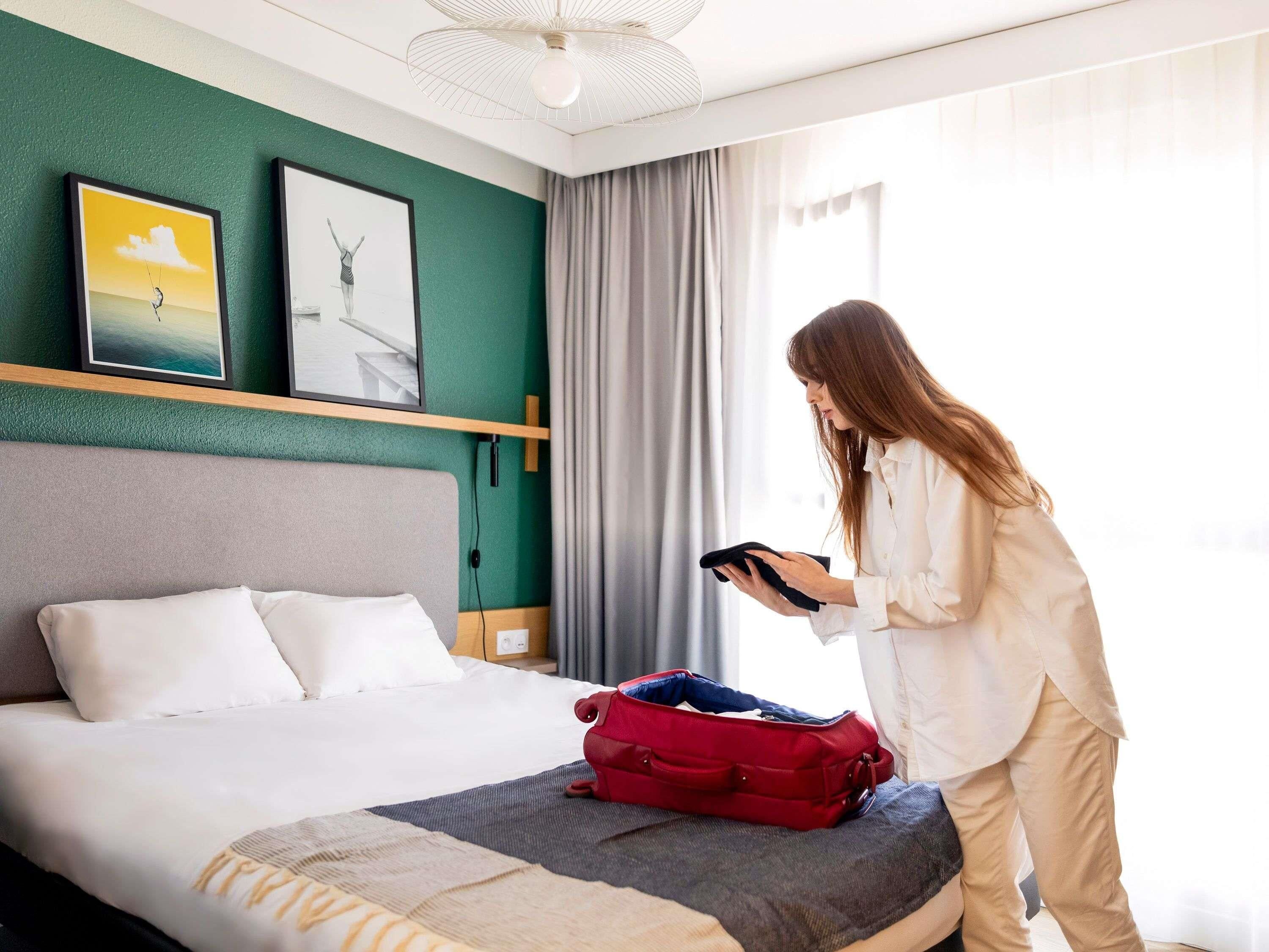 A hotel room with a bed, a red suitcase, and a person using a tablet.