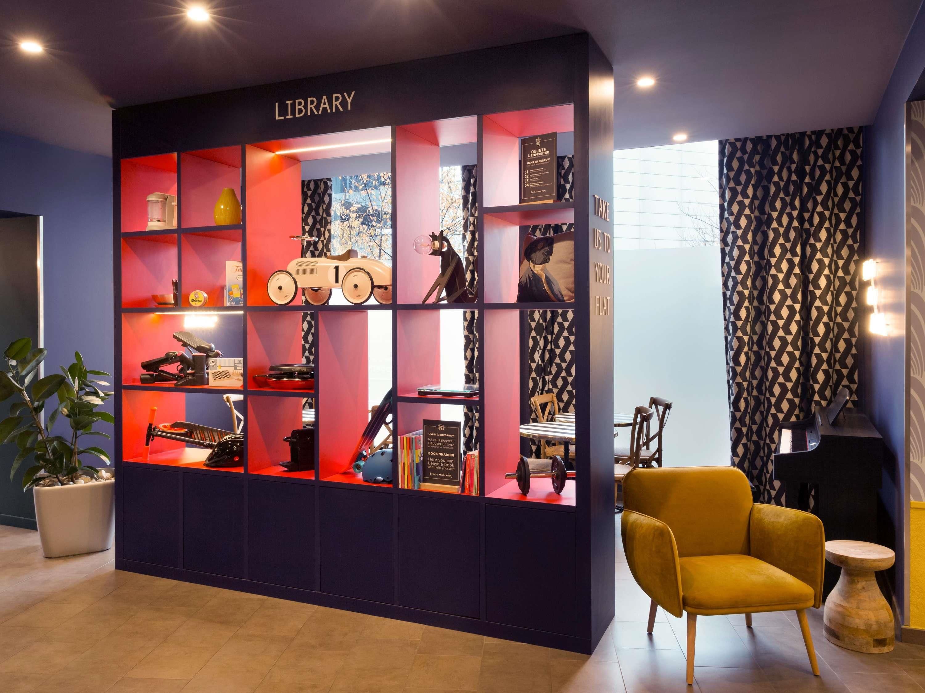 A library with shelves containing various items, a yellow armchair, and a small table.
