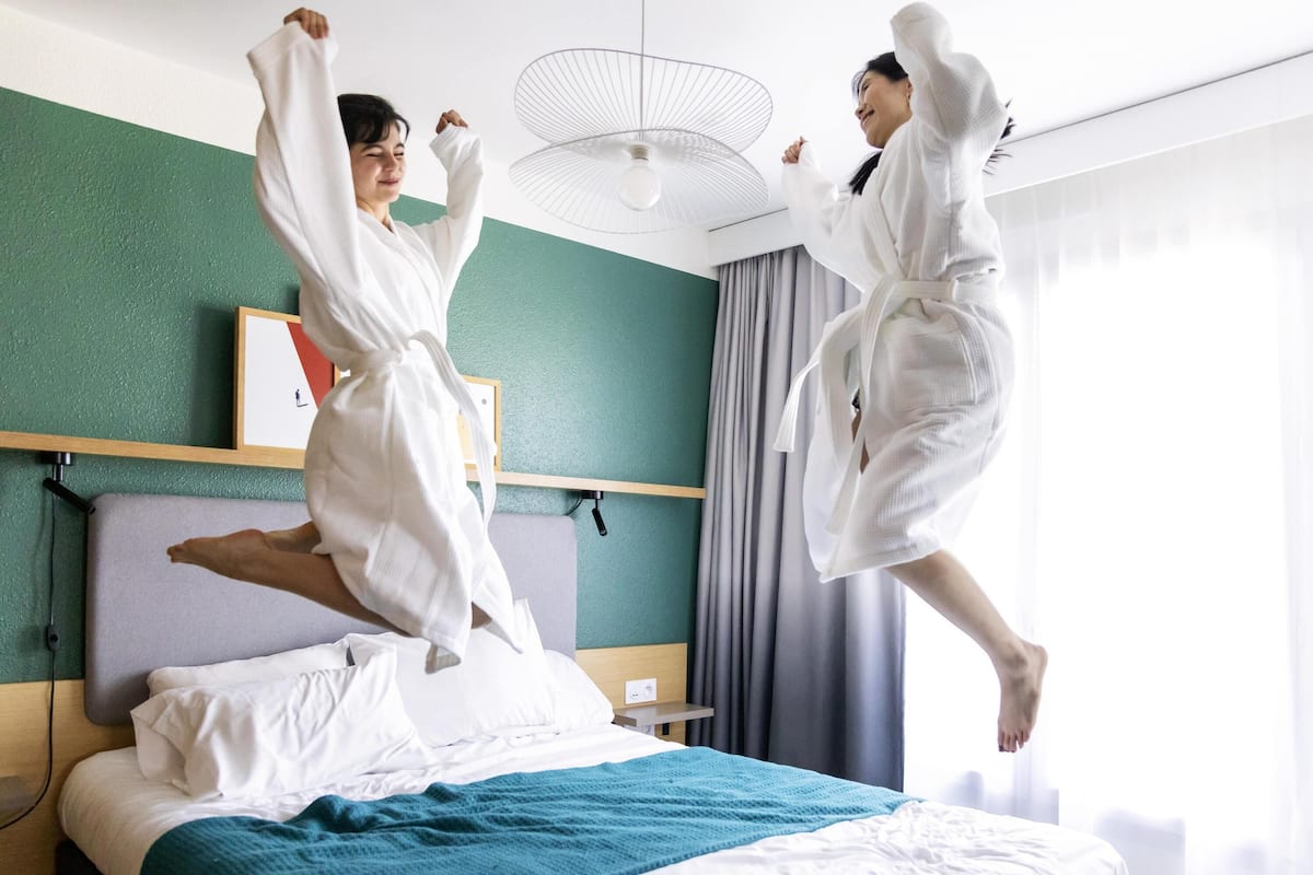 Een hotelkamer met een bed, nachtkastje, een ventilator aan de muur en een raam met gordijnen.