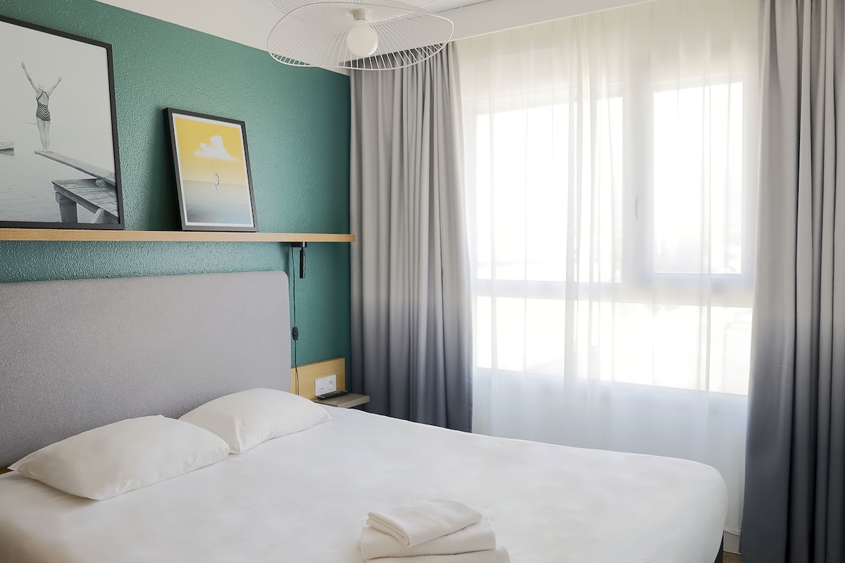 A neatly made bed with white linens, a teal accent wall, and a framed picture above it.