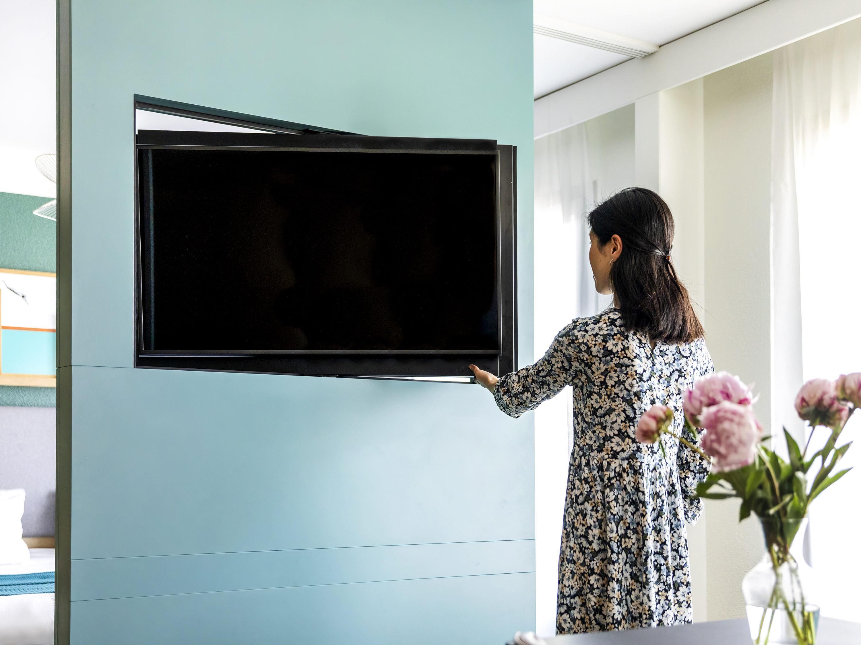A woman adjusting a flat-screen TV mounted on a light blue wall.