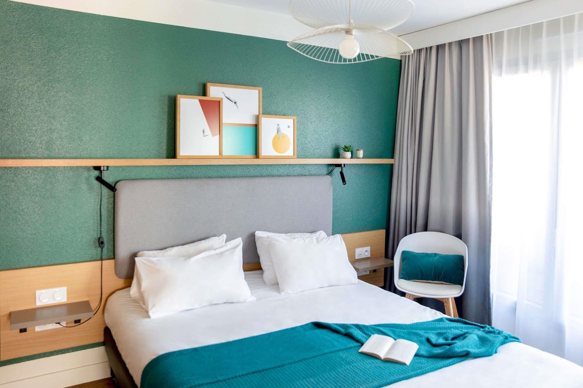 Een hotelkamer met een bed, een stoel, een plank met kunstwerken en een plafondventilator.
