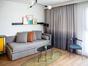 A modern living room with a grey sofa, a small round table, a blue chair, and a black floor lamp.