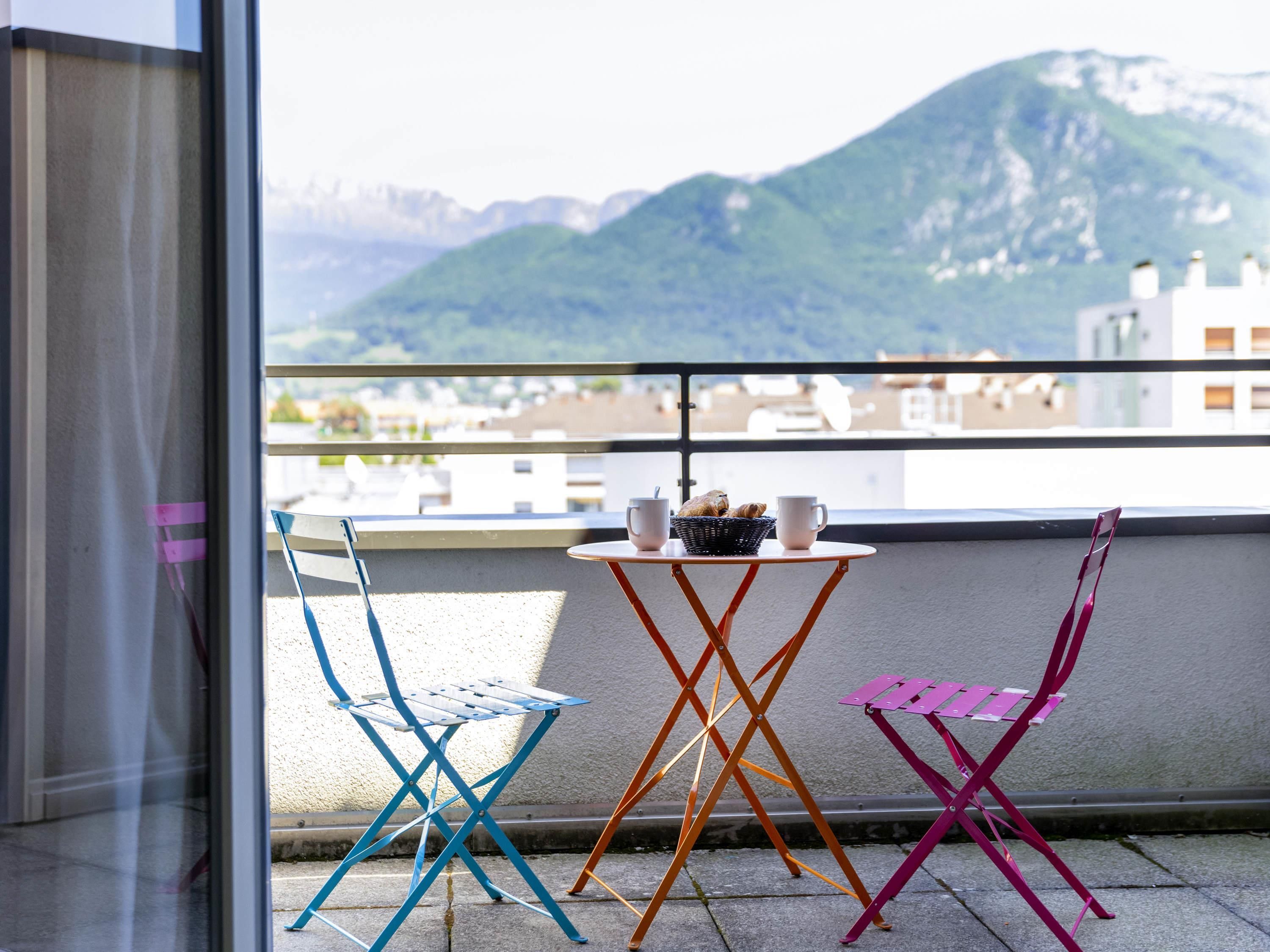 A balcony with three chairs and a table, overlooking a mountainous landscape.