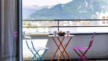 A balcony with three chairs and a table, overlooking a mountainous landscape.