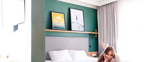 Een hotelkamer met een bed, een bureau met een laptop, een potplant en kunst aan de muur.