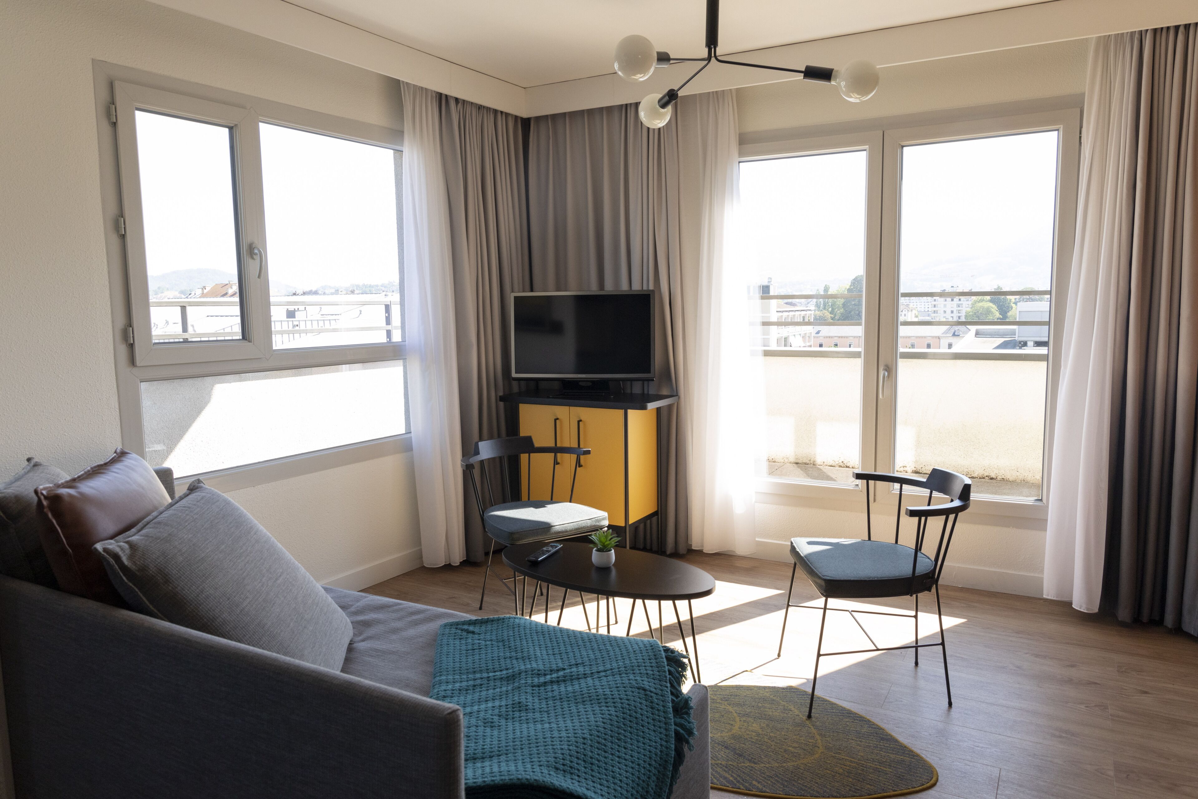 Ein modernes Wohnzimmer mit einer Couch, einem Fernseher, einem kleinen Tisch und zwei Stühlen.