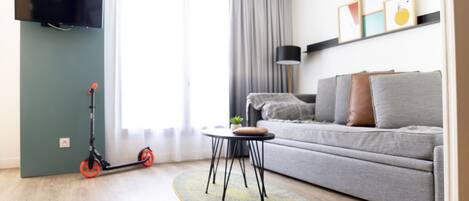 Un salon moderne avec un canapé gris, une petite table ronde, un téléviseur fixé au mur et un scooter.