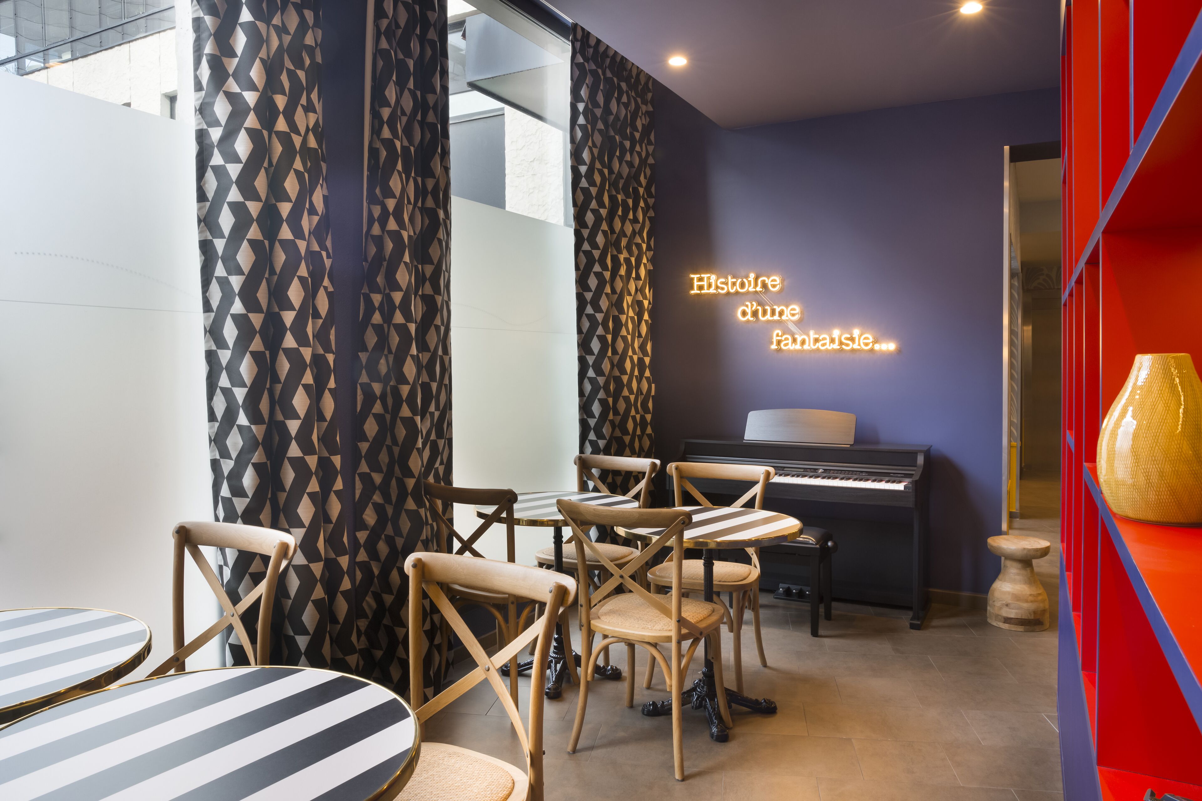 Un espace repas avec des tables et des chaises à rayures, un piano et un panneau lumineux au néon.