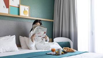 Een hotelkamer met een bed, een nachtkastje met een ontbijttafel, een krant en kunst aan de muur.