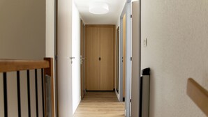 Een gang met houten vloer, een houten deur aan het einde en een lamp aan het plafond.