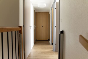 Een gang met houten vloer, een houten deur aan het einde en een lamp aan het plafond.