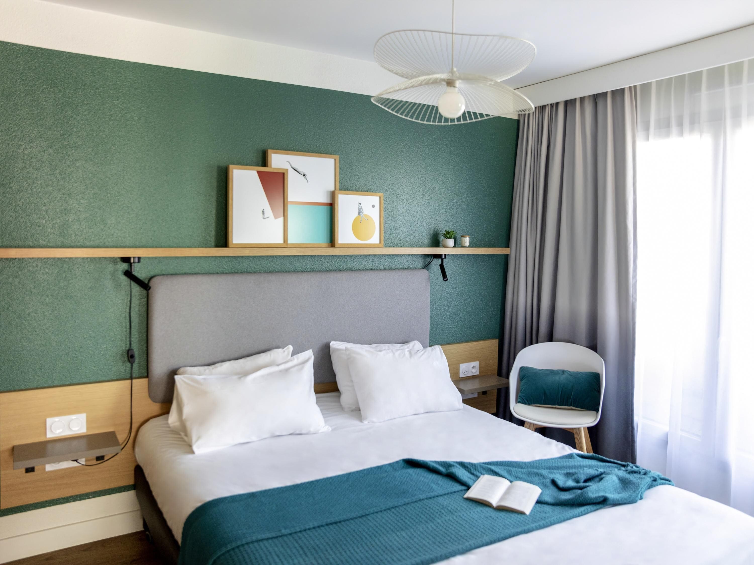 A hotel room with a bed, a bedside table, a chair, a ceiling fan, and artwork on the wall.