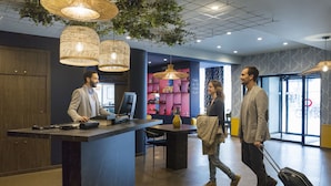 A reception desk with a computer, a seating area, and a decorative wall with a sign. - Aparthotel Adagio Annecy Centre (Annecy)