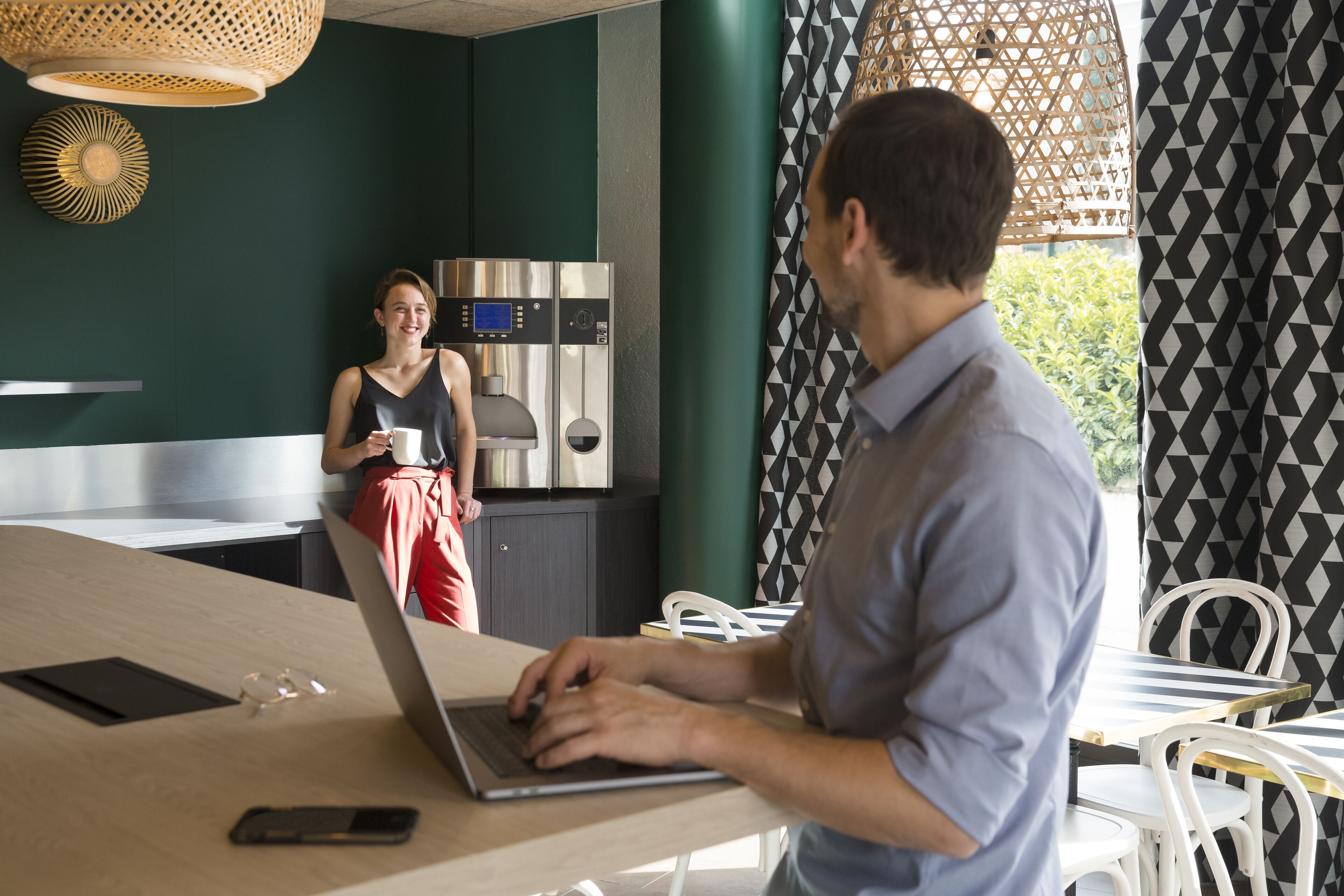 Une cuisine moderne avec des appareils en acier inoxydable, un ordinateur portable sur une table et une personne qui travaille.