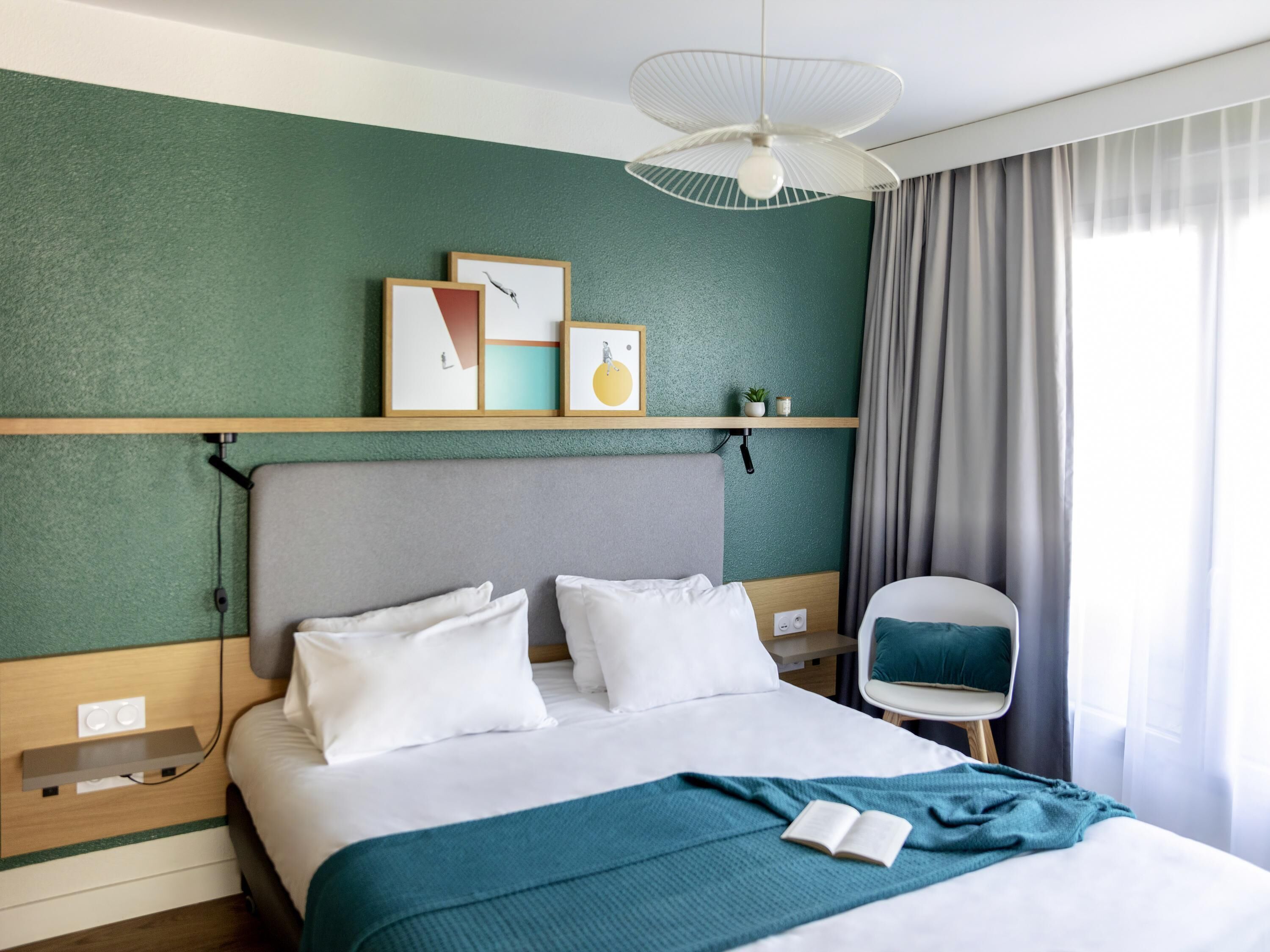 Een hotelkamer met een bed, nachtkastje, stoel, plafondventilator en kunst aan de muur.