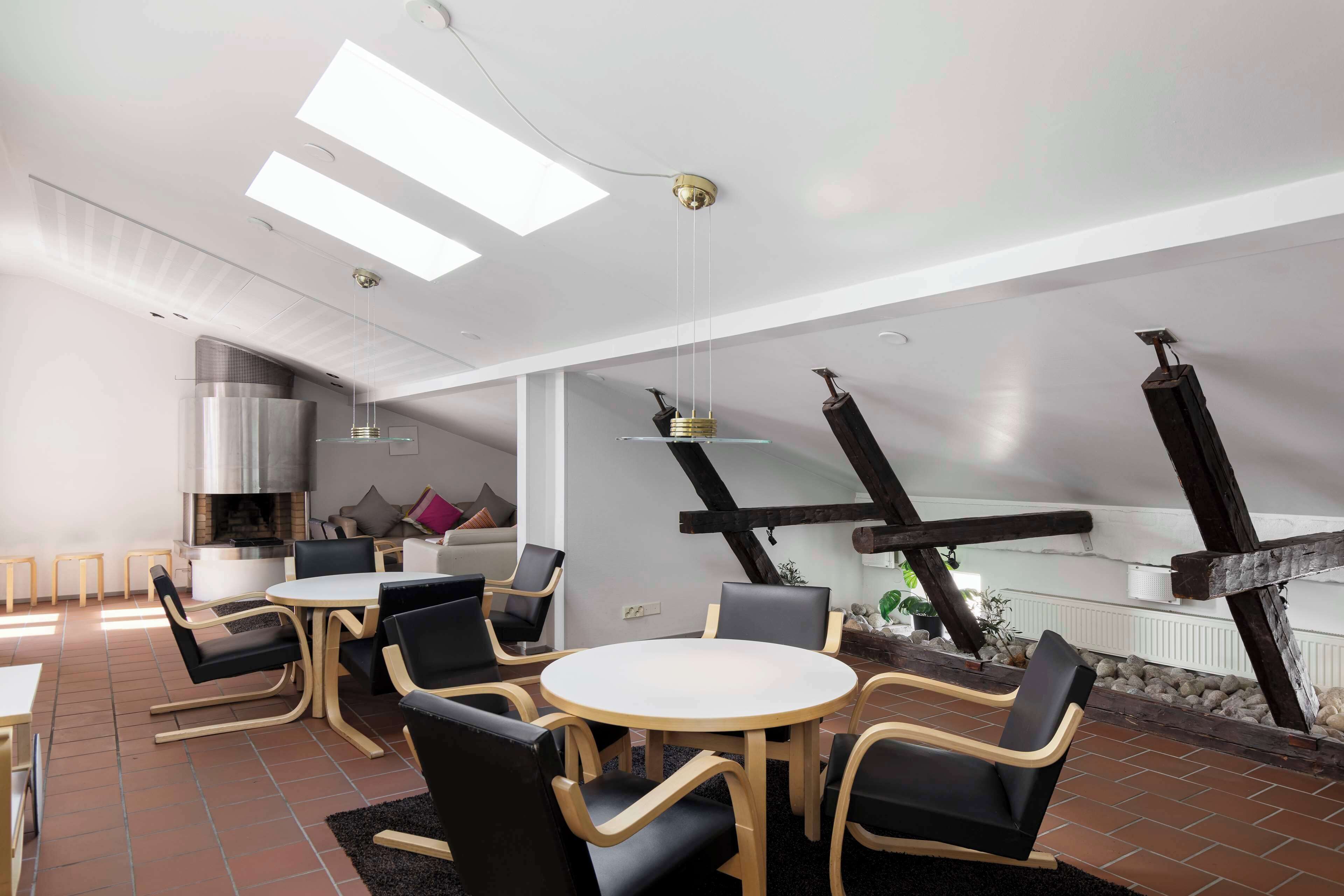 A modern interior with a round dining table, black and wooden chairs, a fireplace, and exposed wooden beams.