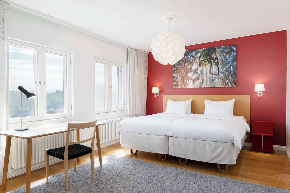 Une chambre à coucher avec un grand lit, un bureau et une chaise. Il y a deux tables de chevet avec des lampes.