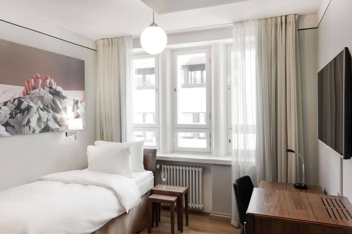 Une chambre d’hôtel équipée d’un lit, d’un bureau, d’une chaise, d’une télévision, d’une fenêtre avec des rideaux et d’un radiateur.