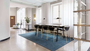 A modern hotel lobby with a dining area featuring a long table, chairs, and a blue patterned rug. - Radisson Blu Aleksanteri Hotel, Helsinki (Helsinki)
