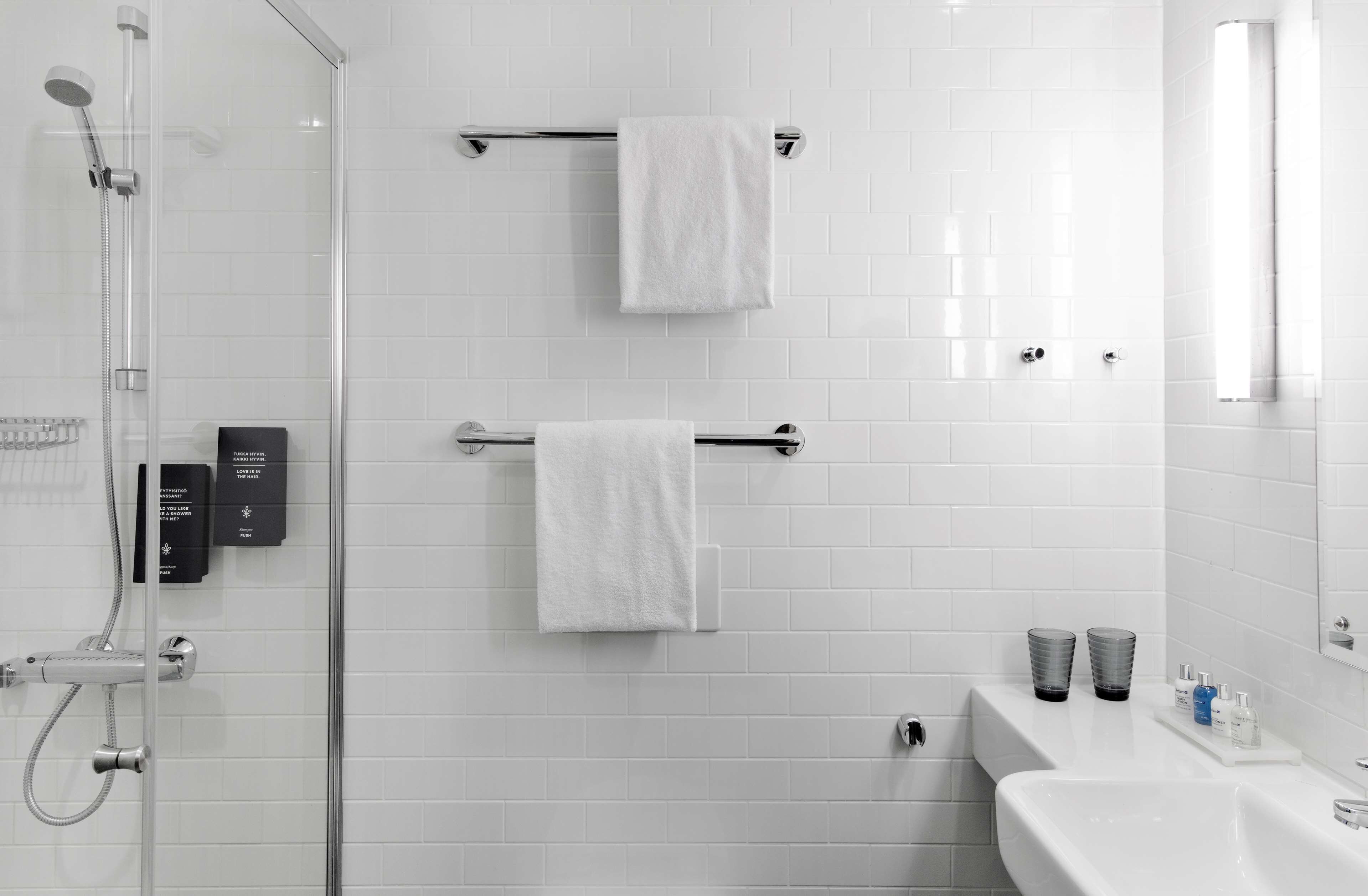 Un baño moderno con cabina de ducha de vidrio, dos toalleros con toallas blancas, un lavabo blanco con espejo y un estante con artículos de aseo.