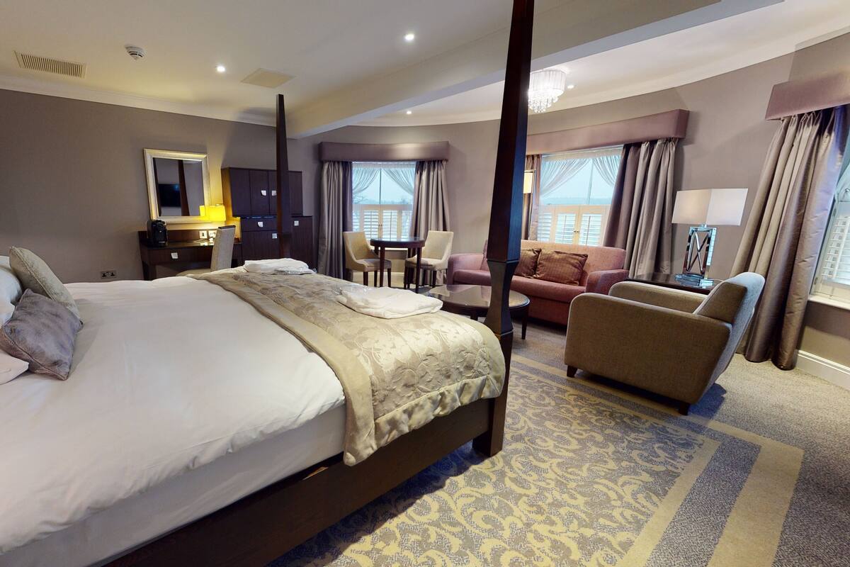A hotel room with a large bed, a desk, a chair, a sofa, and a view of the city.
