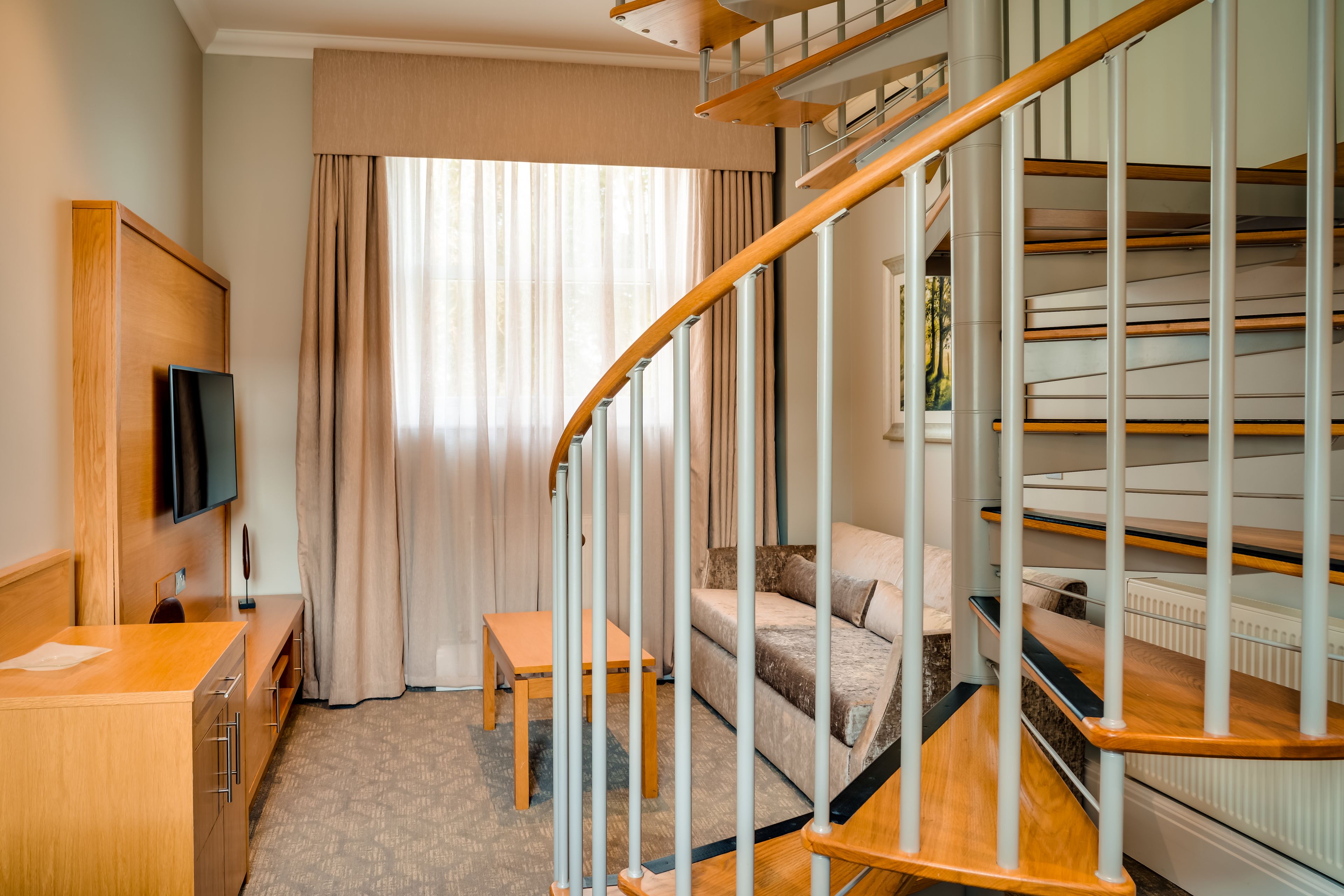 Une chambre d’hôtel avec un bureau en bois, une télévision, un canapé et un escalier.