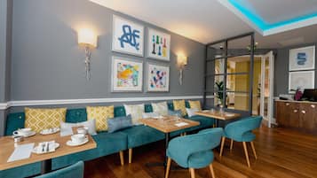 Un comedor moderno con sofás azul turquesa, mesas de madera y obras de arte en las paredes.