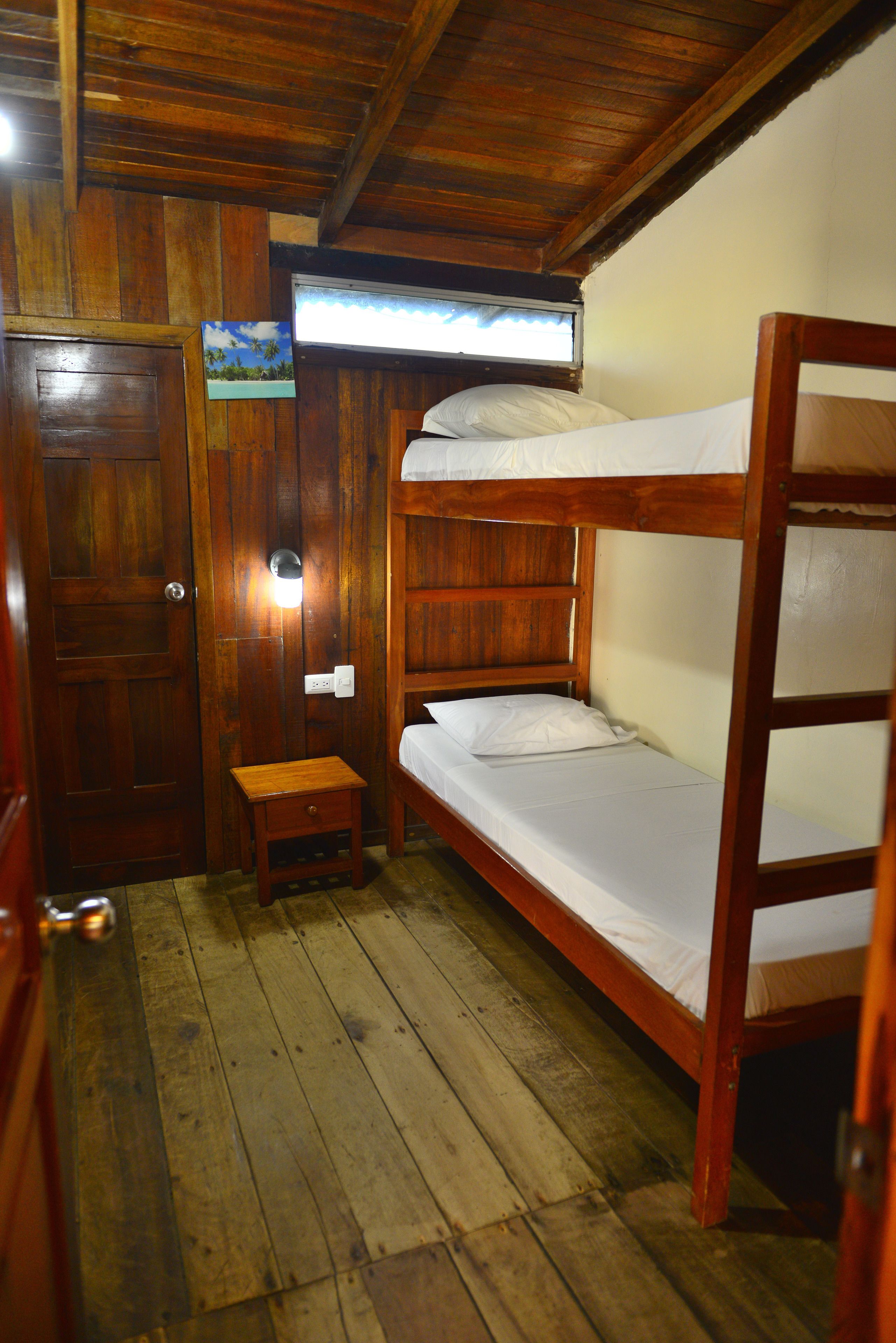 Habitación con una cama litera de madera, una mesita de noche de madera y una puerta.