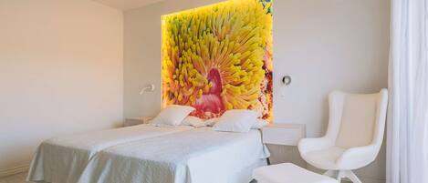 A modern bedroom with a large bed, a white chair, and a unique wall mural.