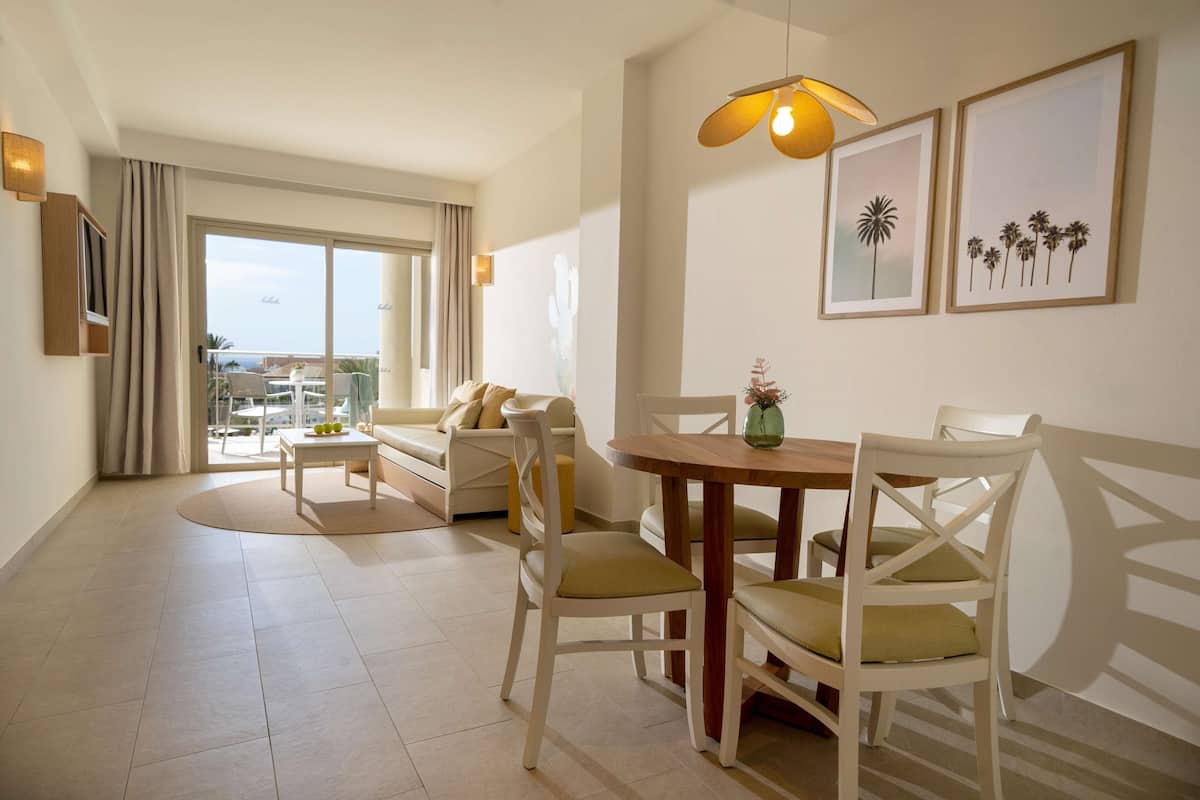 Un salon moderne comprenant un canapé, une table à manger et des chaises, une grande fenêtre avec des rideaux et une vue sur l’extérieur.