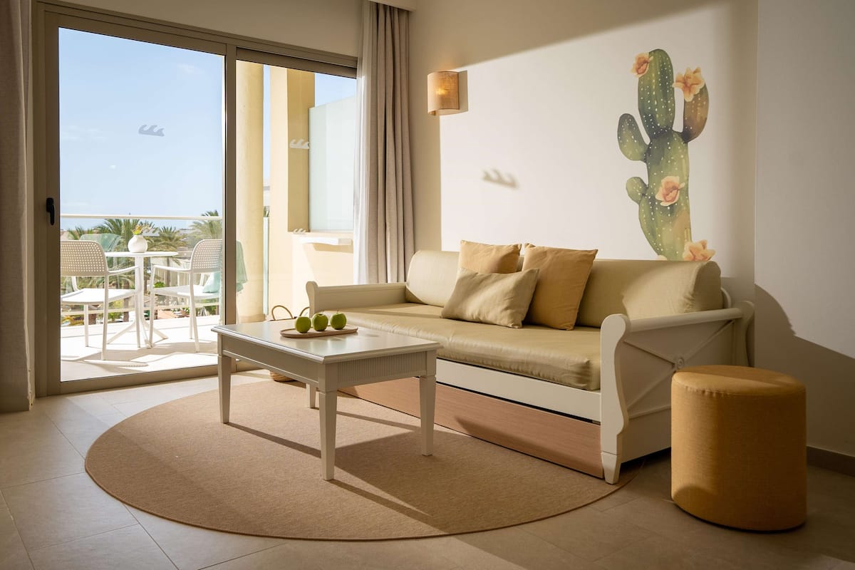 Un salon avec un canapé, une table basse sur laquelle sont posées des pommes, un tapis rond et une décoration murale représentant un cactus.