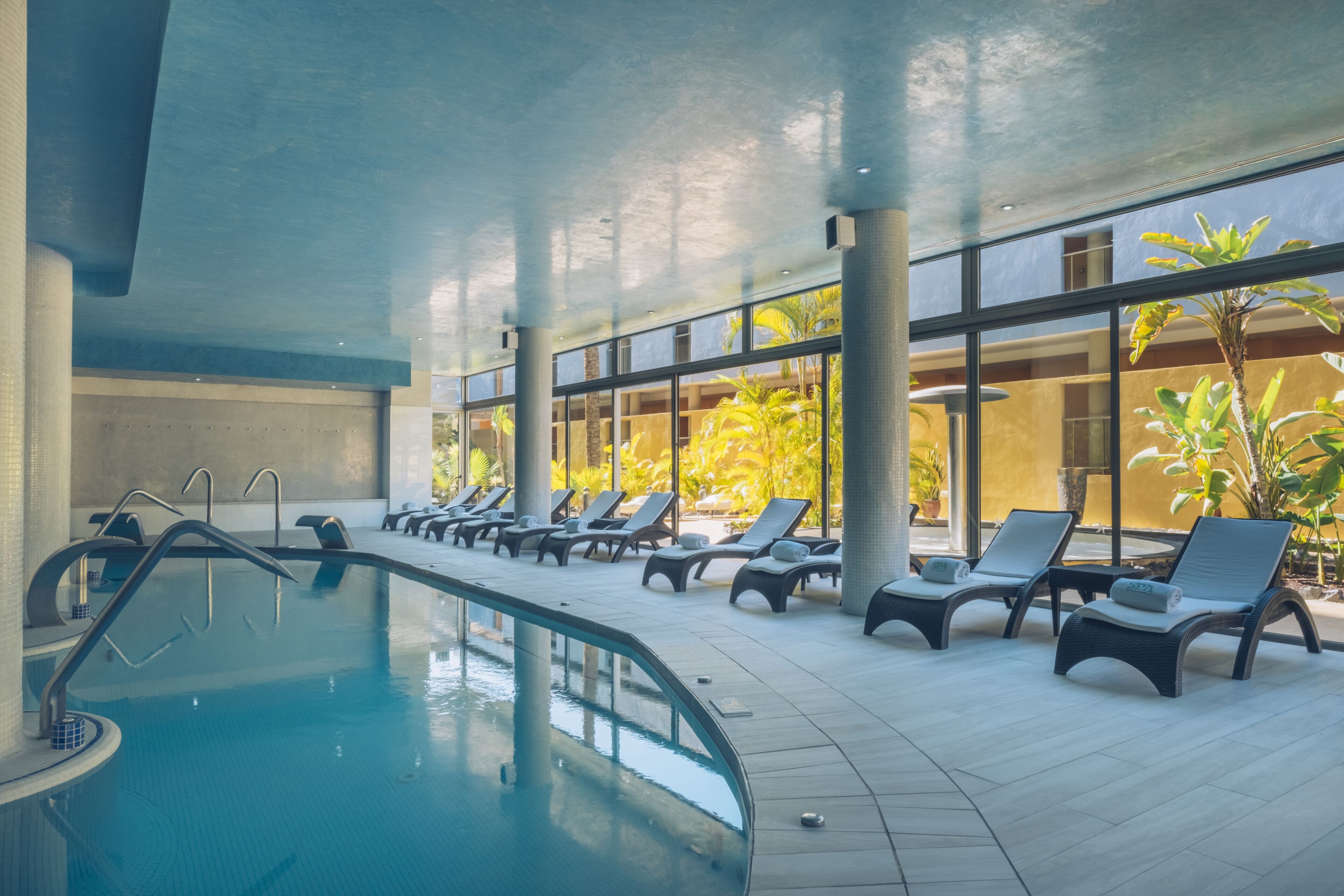 Zona de piscina con sillas de descanso y amplias ventanas.