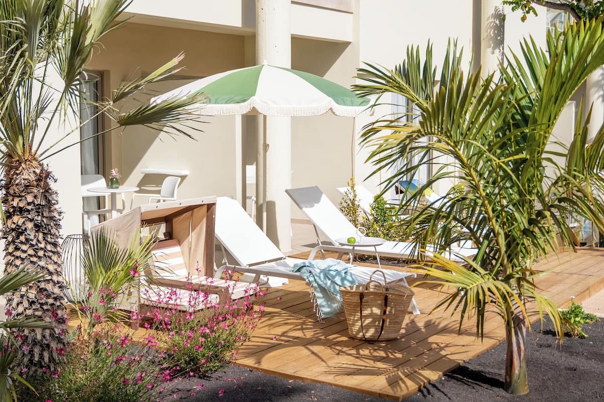 Un espace extérieur ensoleillé, aménagé avec des fauteuils confortables, une table et un parasol vert et blanc.
