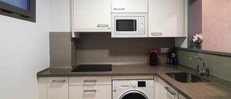 A compact kitchen with white cabinets, a microwave, a built-in washing machine, a sink, and a window with a view.
