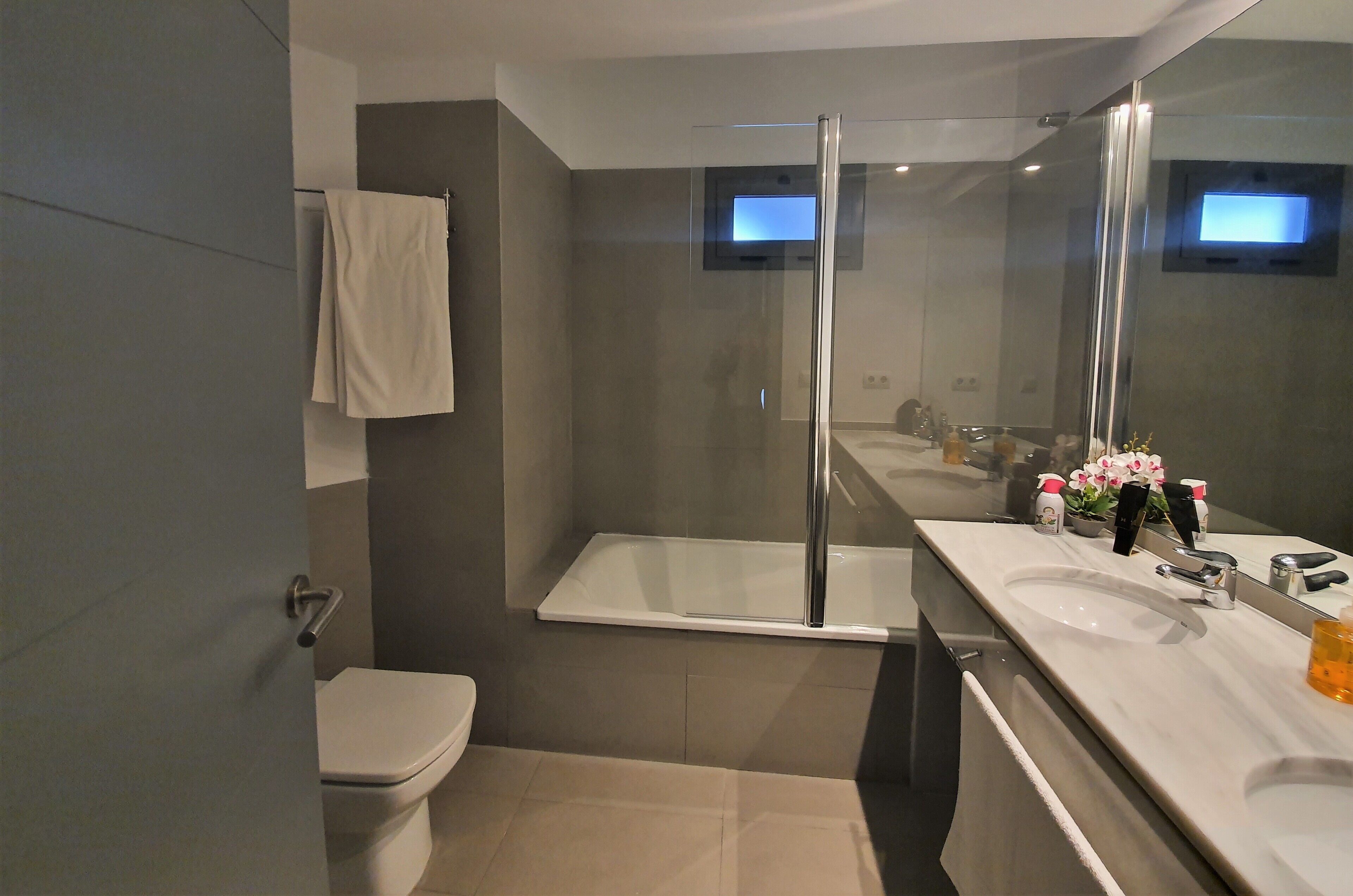 Un baño moderno con ducha envuelta en vidrio, inodoro blanco y tocador con espejo y lavabo.