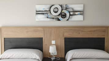 A hotel room with a wooden headboard, two beds, a nightstand with a lamp, and a wall-mounted abstract artwork.